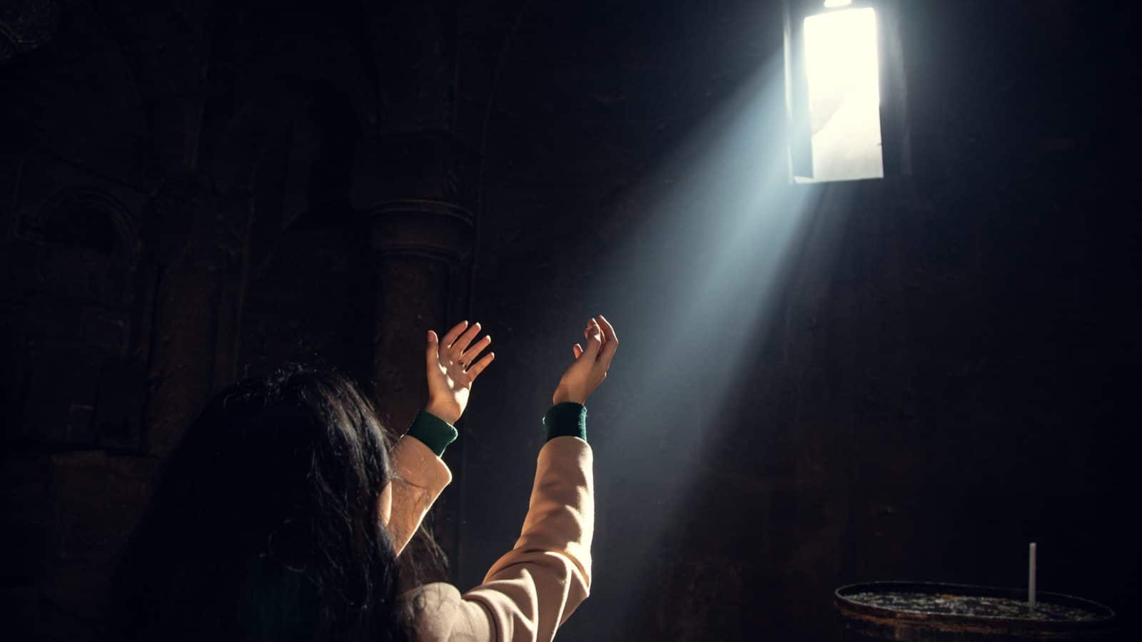 Vrouw bidt met opgeheven handen in een lichtstraal, beeld bij Hoe moet ik bidden
